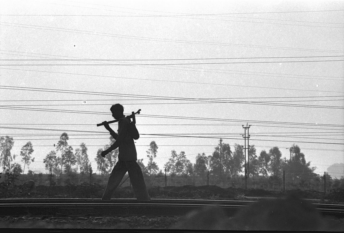 The silhouette of a man carrying a load on his shoulder, walking under power lines at dusk.