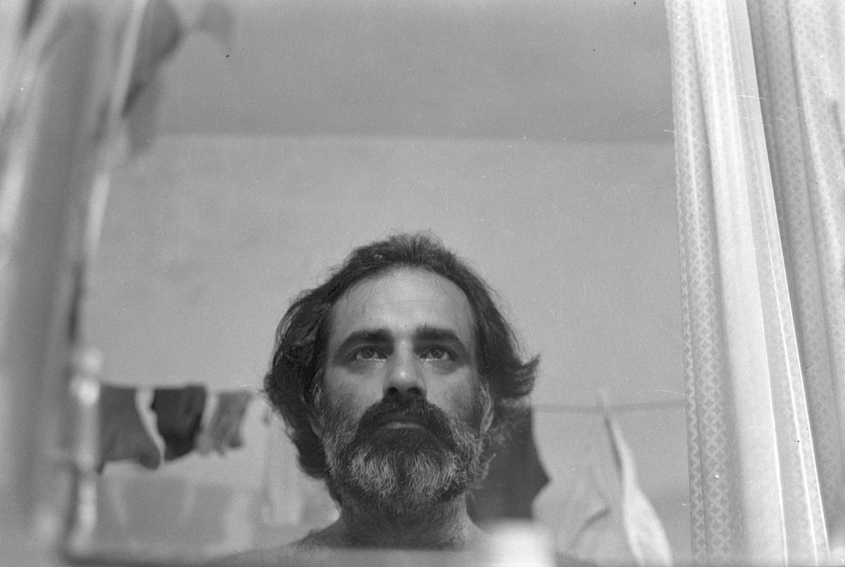 A bearded man looking straight into the camera, washing hanging on a line behind him.